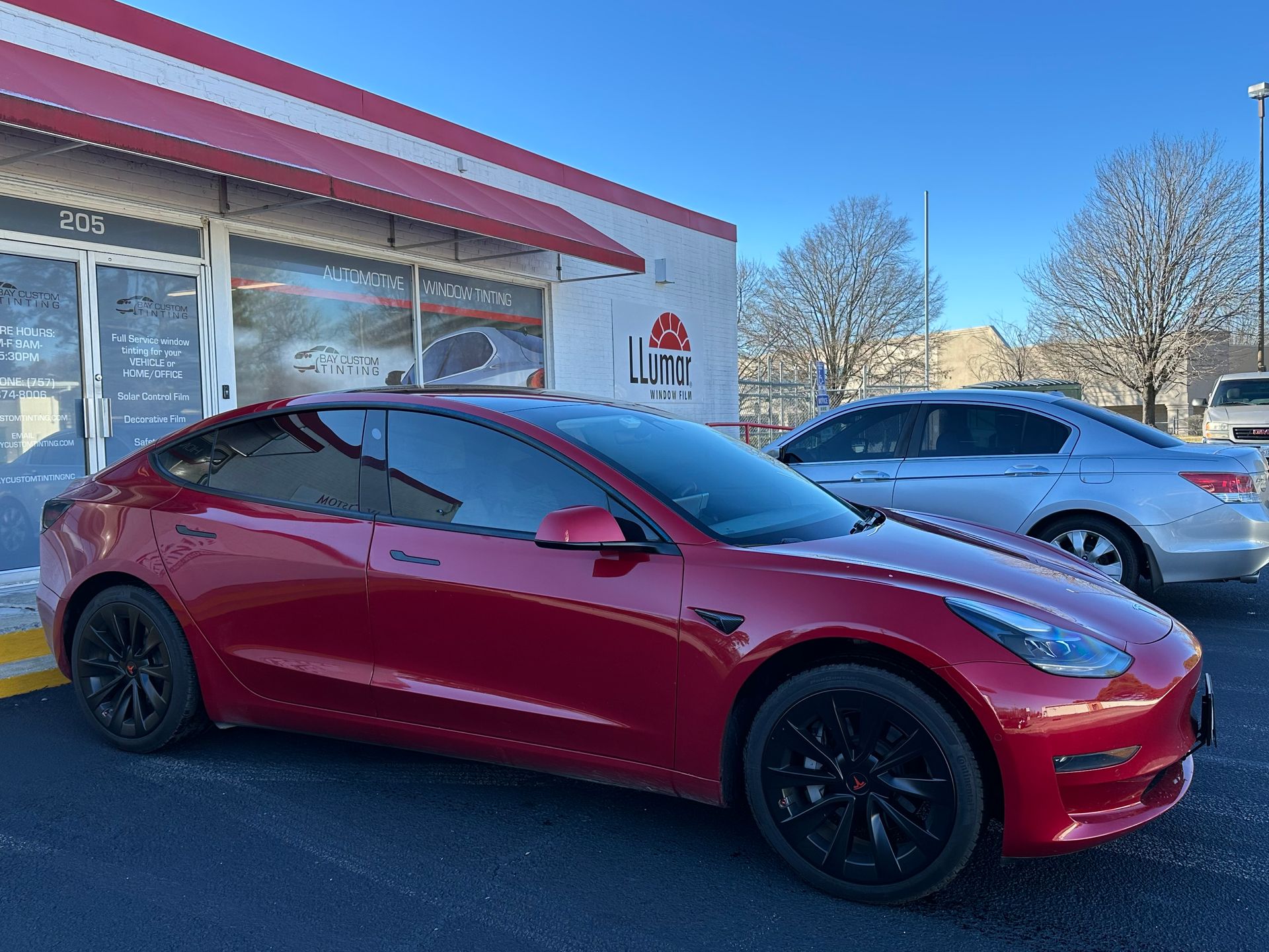 A red tesla model 3 is parked in front of a car dealership.