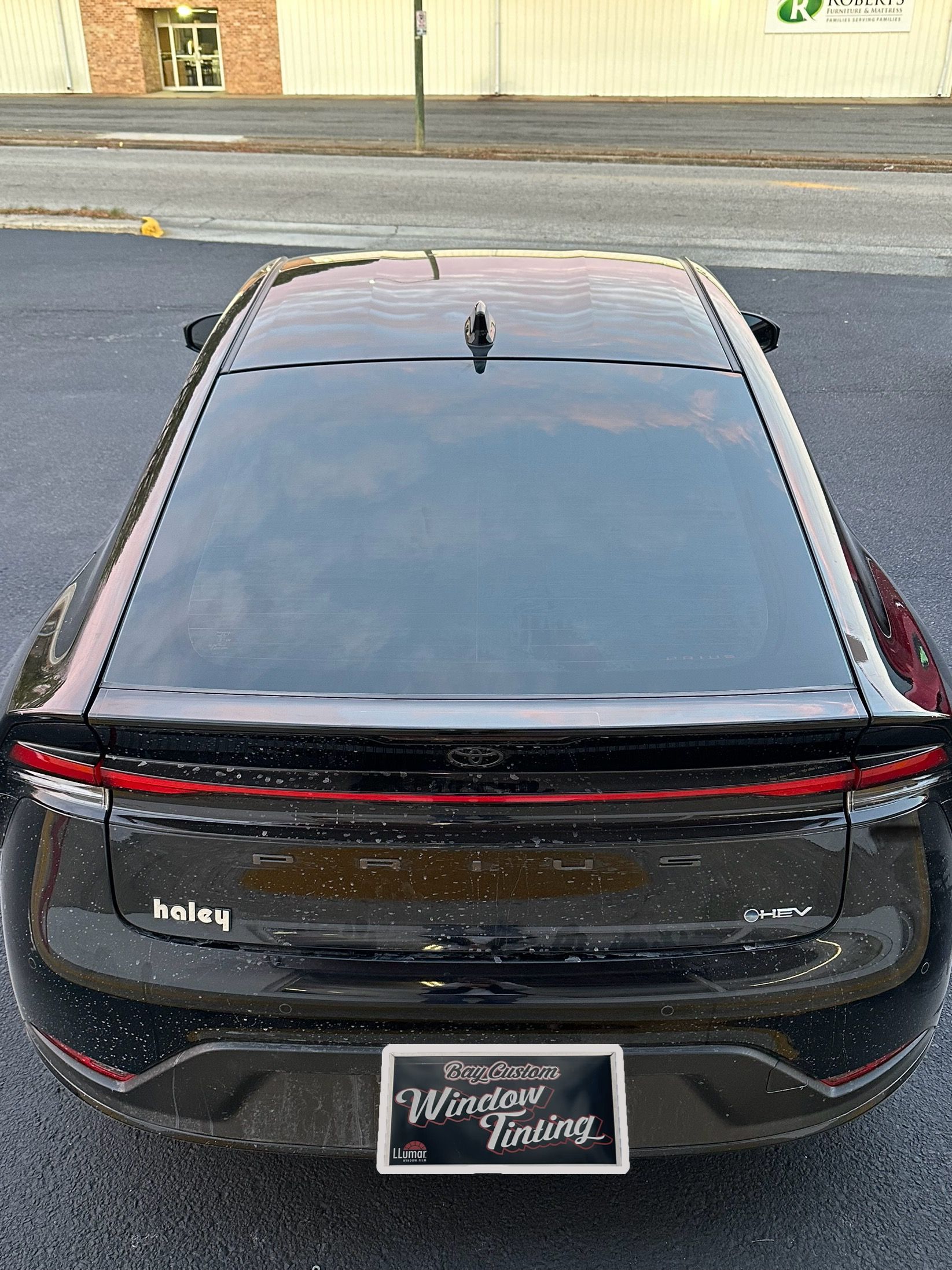 A black car is parked on the side of the road in front of a building.