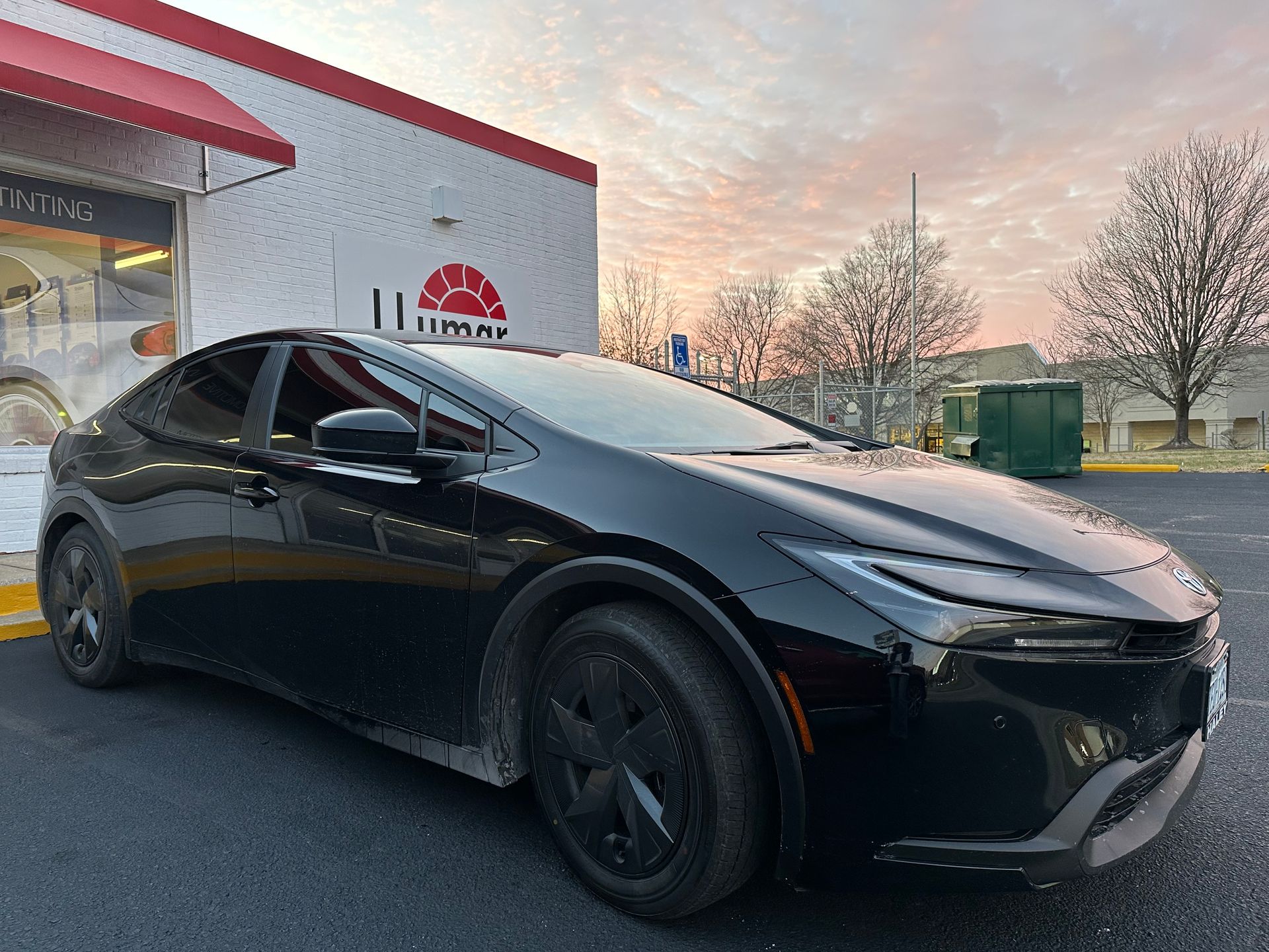 A black car is parked in front of a building with a red awning.