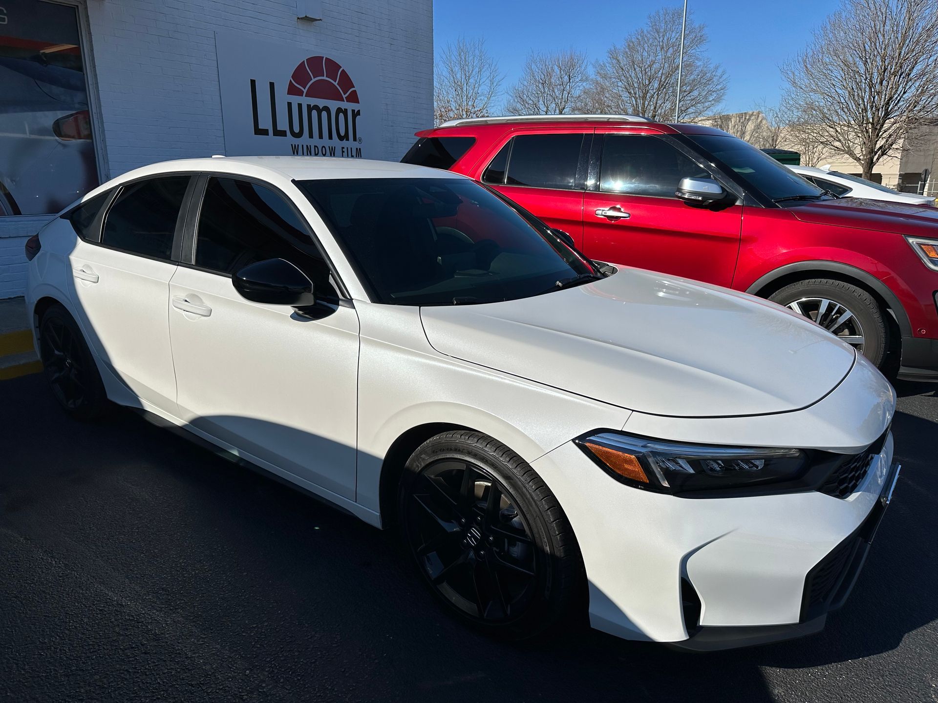 A white car is parked next to a red car in a parking lot.