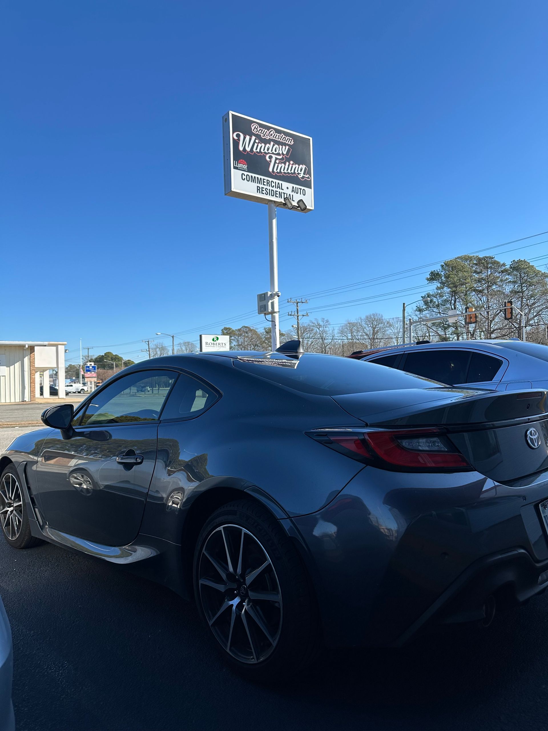 A black sports car is parked in front of a large sign.