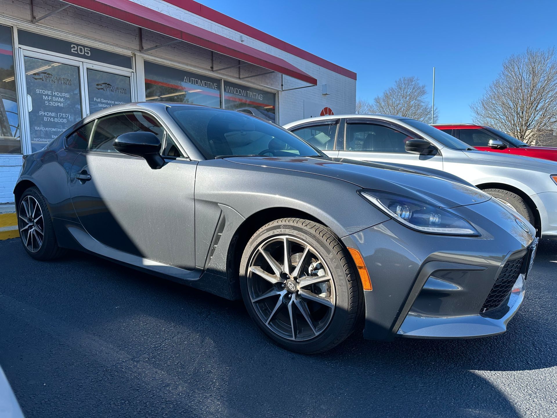 A gray sports car is parked in front of a car dealership.