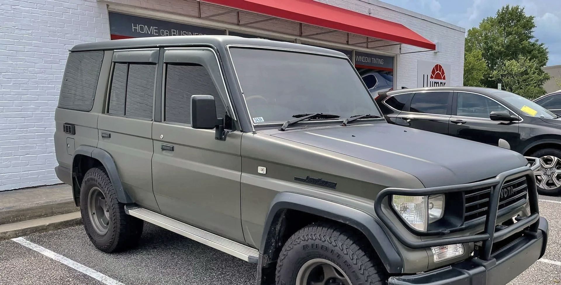 A green jeep is parked in a parking lot in front of a building.