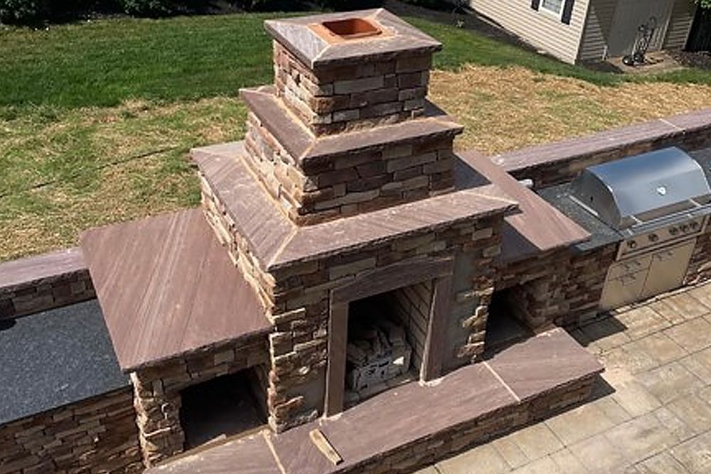 A stone fireplace with a grill in the backyard of a house.