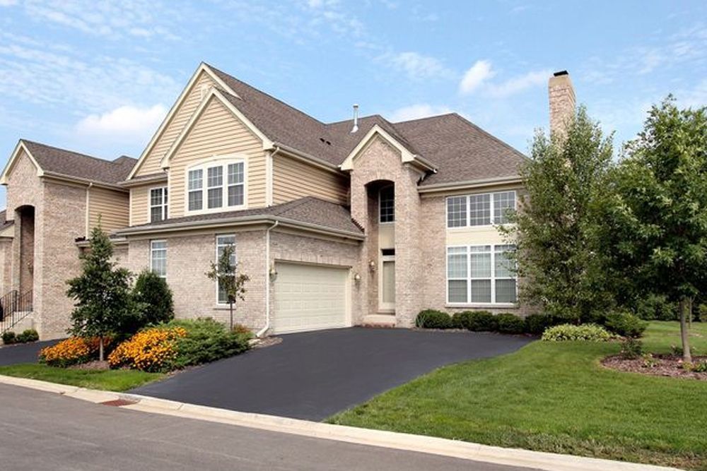 A large brick house with a driveway and trees in front of it.