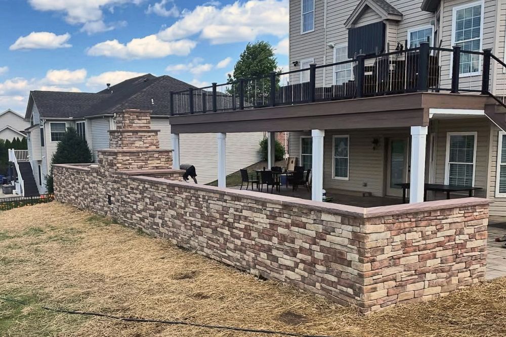 A house with a deck and a stone wall in front of it.
