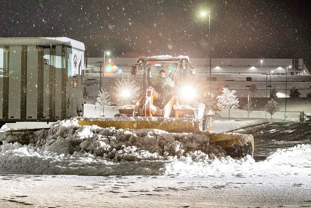 A snow plow is clearing snow from a parking lot at night