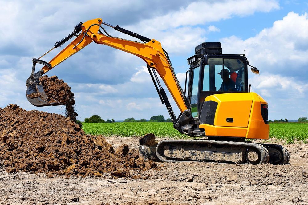 A yellow excavator is digging a pile of dirt in a field.