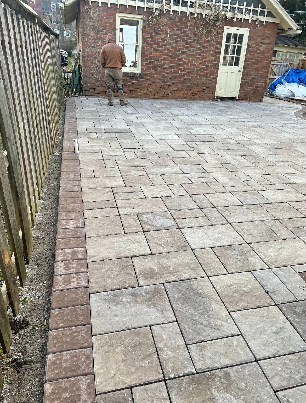 A man is standing on a brick driveway in front of a brick building.
