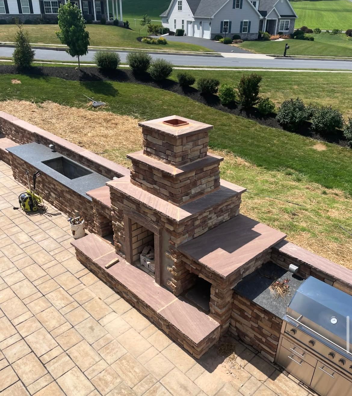 A brick fireplace is sitting on top of a brick patio next to a stainless steel grill.
