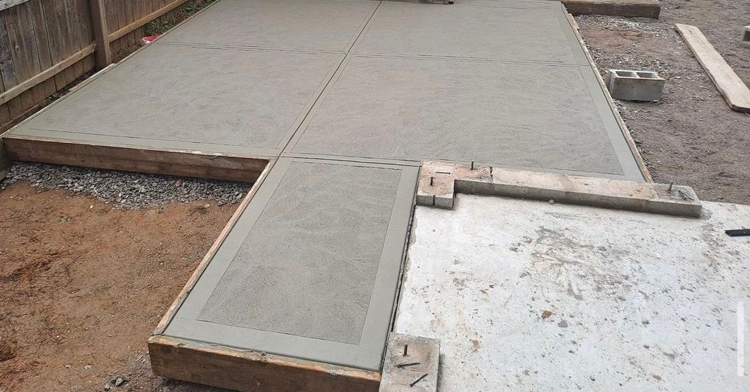 A concrete patio is being built in the backyard of a house.
