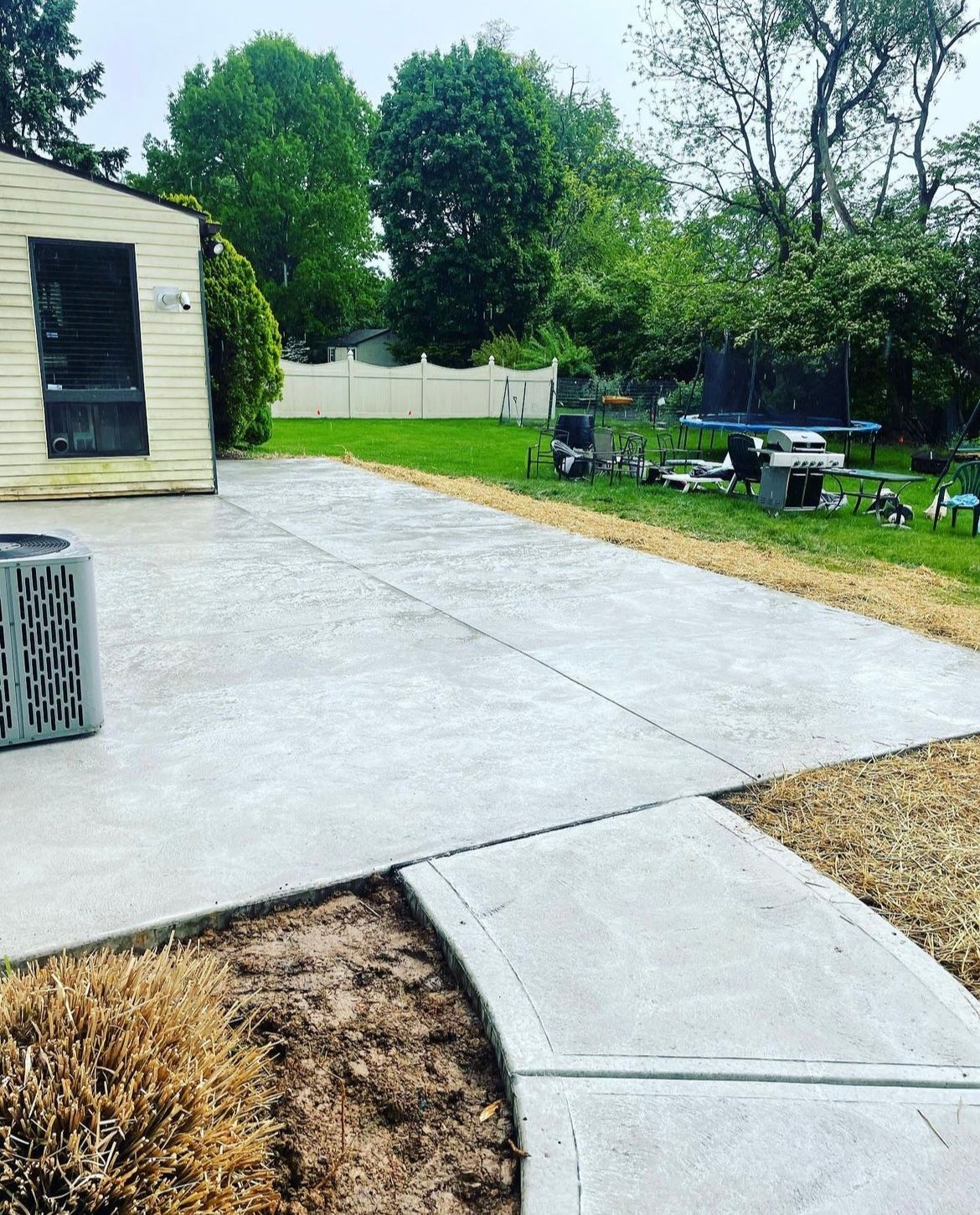 A concrete walkway leading to a house with a shed in the background.