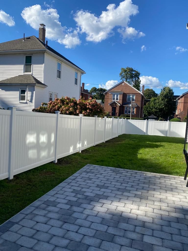 Backyard with white fence, green lawn, and gray paver patio under a blue sky
