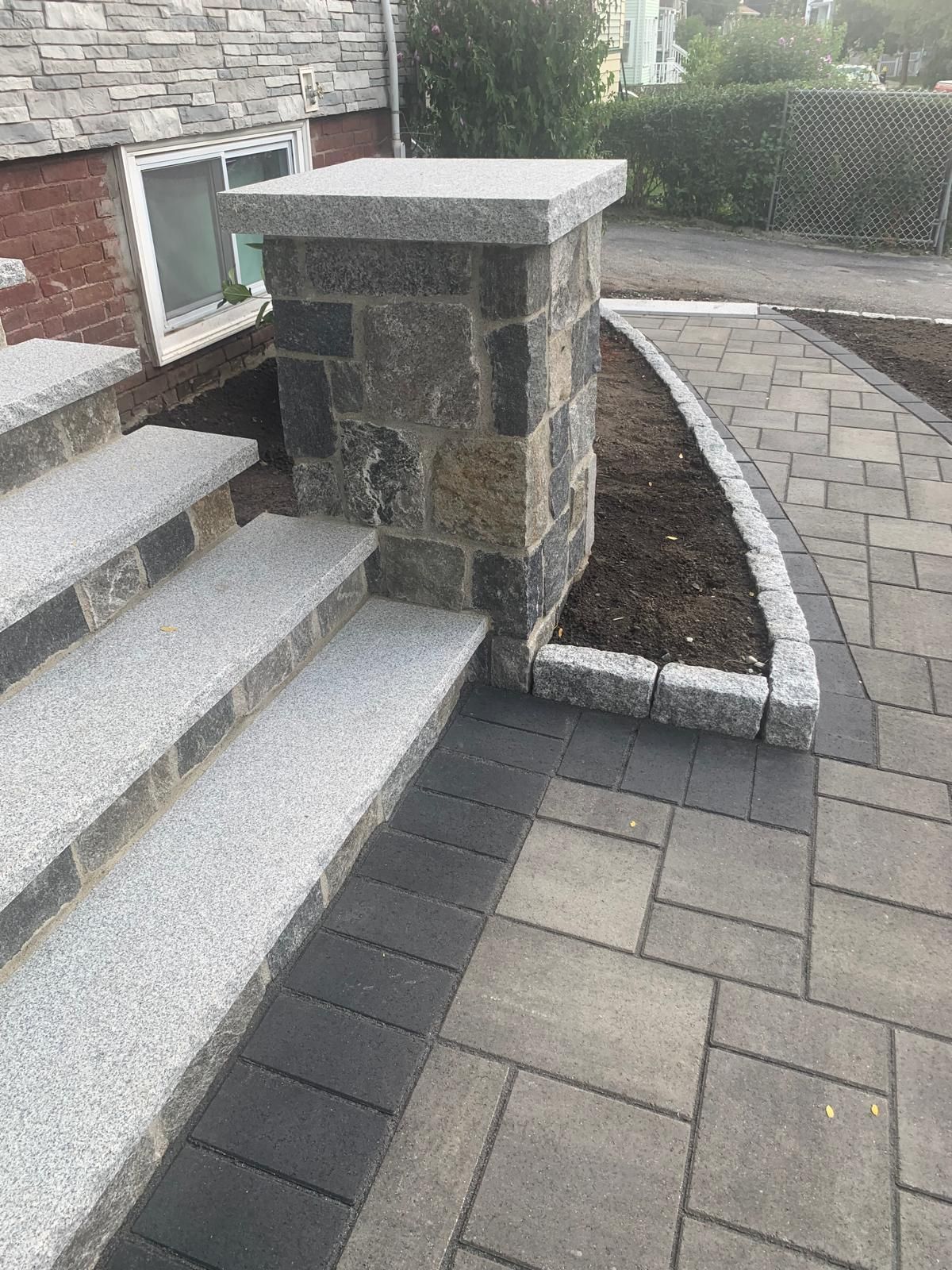 Stone steps and a patio beside a house, with a short masonry pillar and a curved walkway.