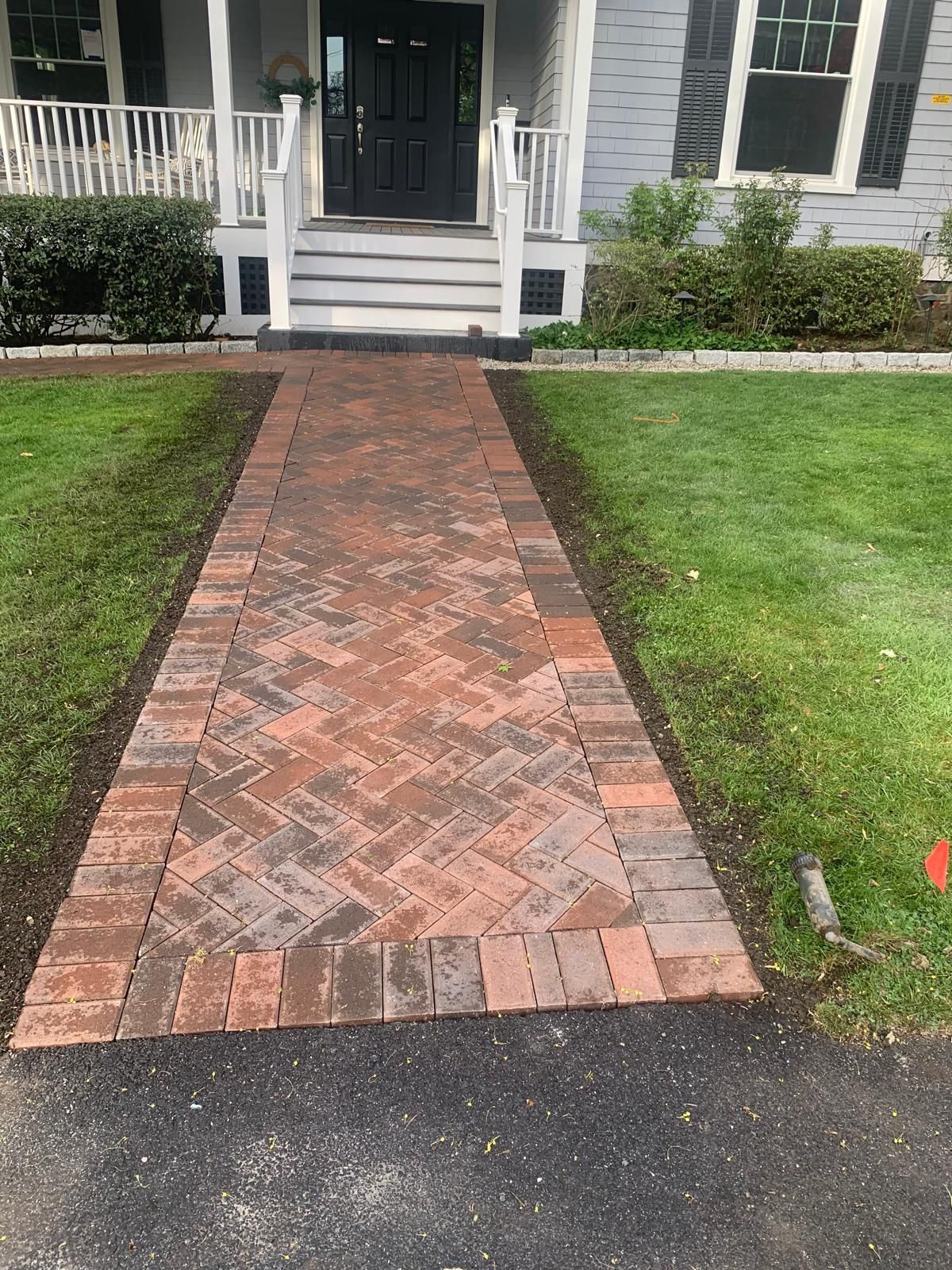 Brick walkway leading to a white house porch through a green lawn.