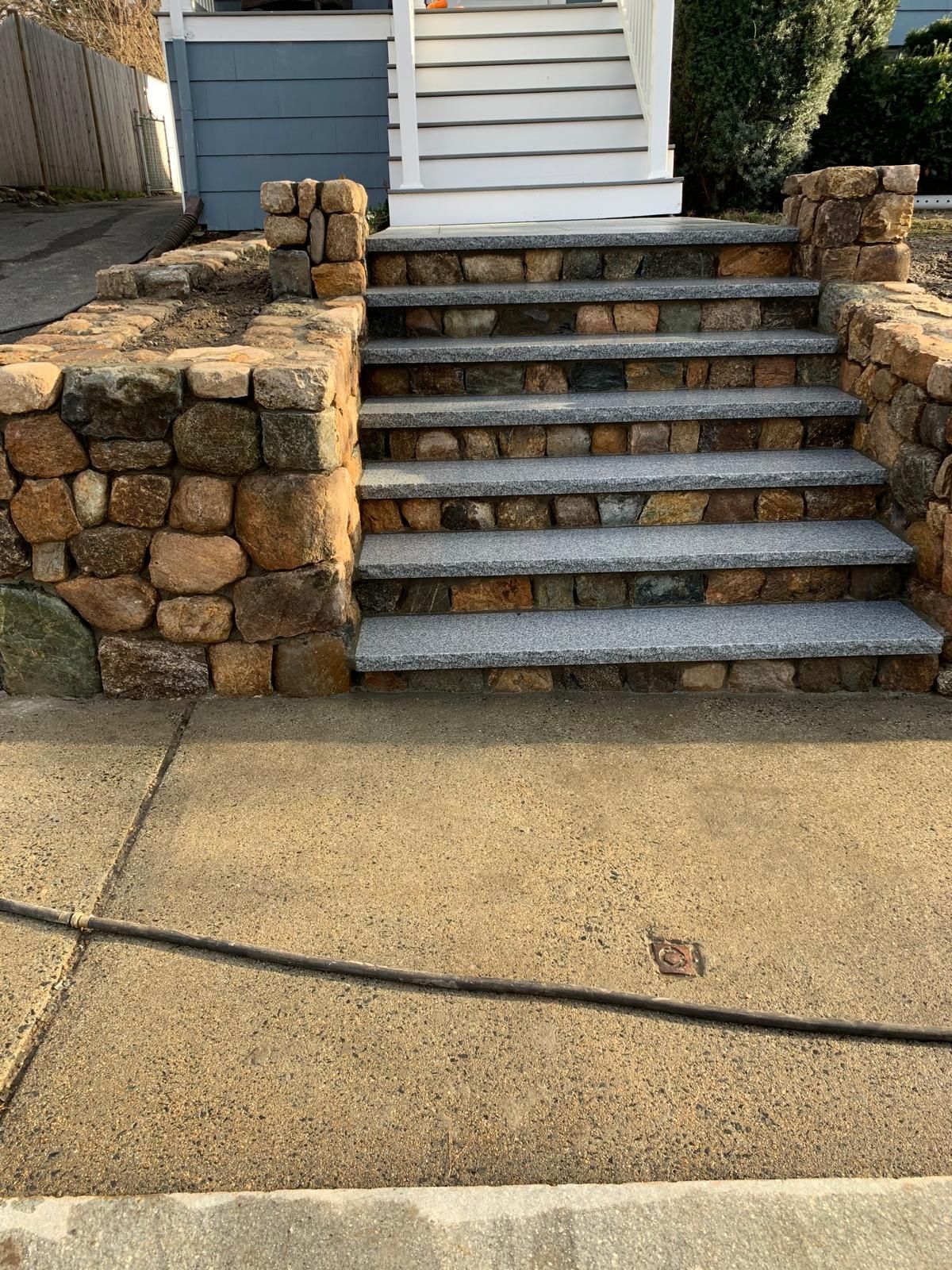 Stone front steps with a short retaining wall and concrete walkway in front of a house