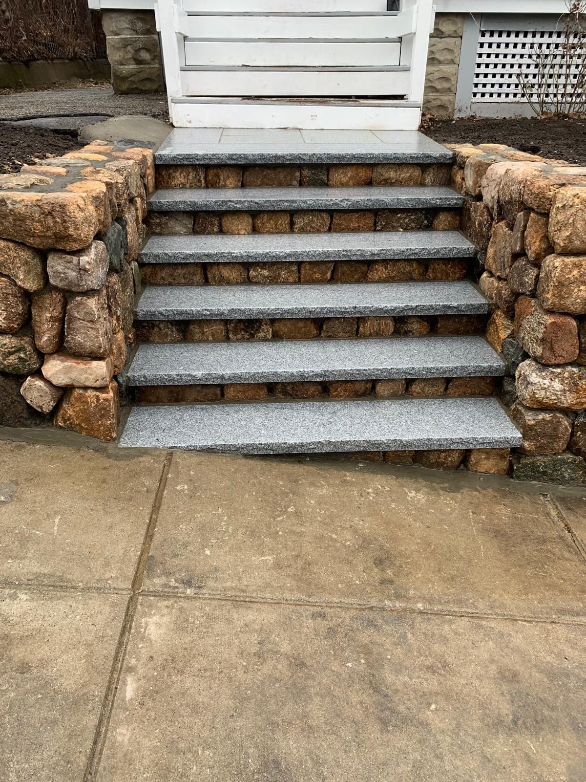 Front steps with stone side walls leading to a white house entrance over a concrete walkway