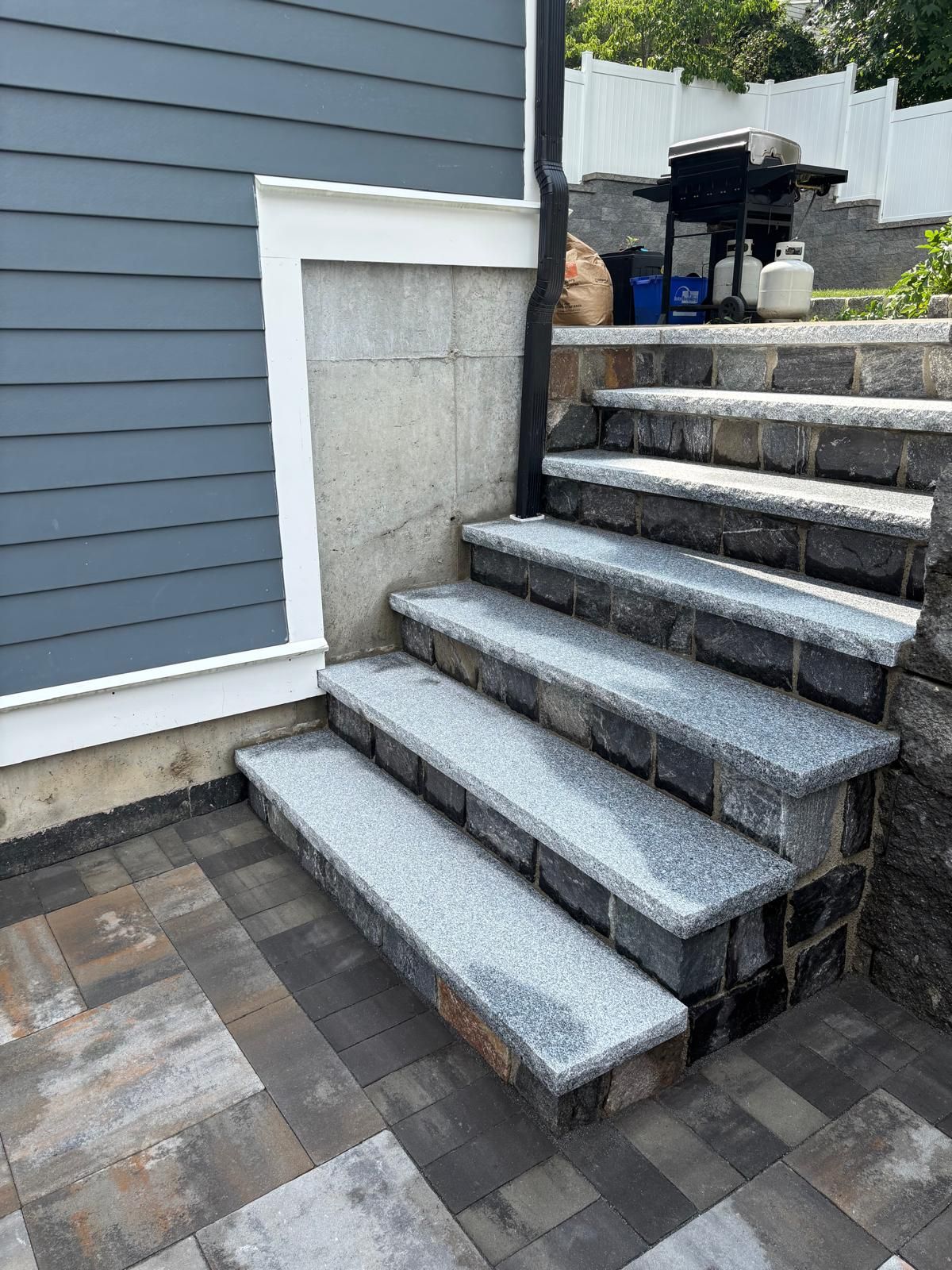Granite outdoor stairs beside a gray house wall and patio pavers