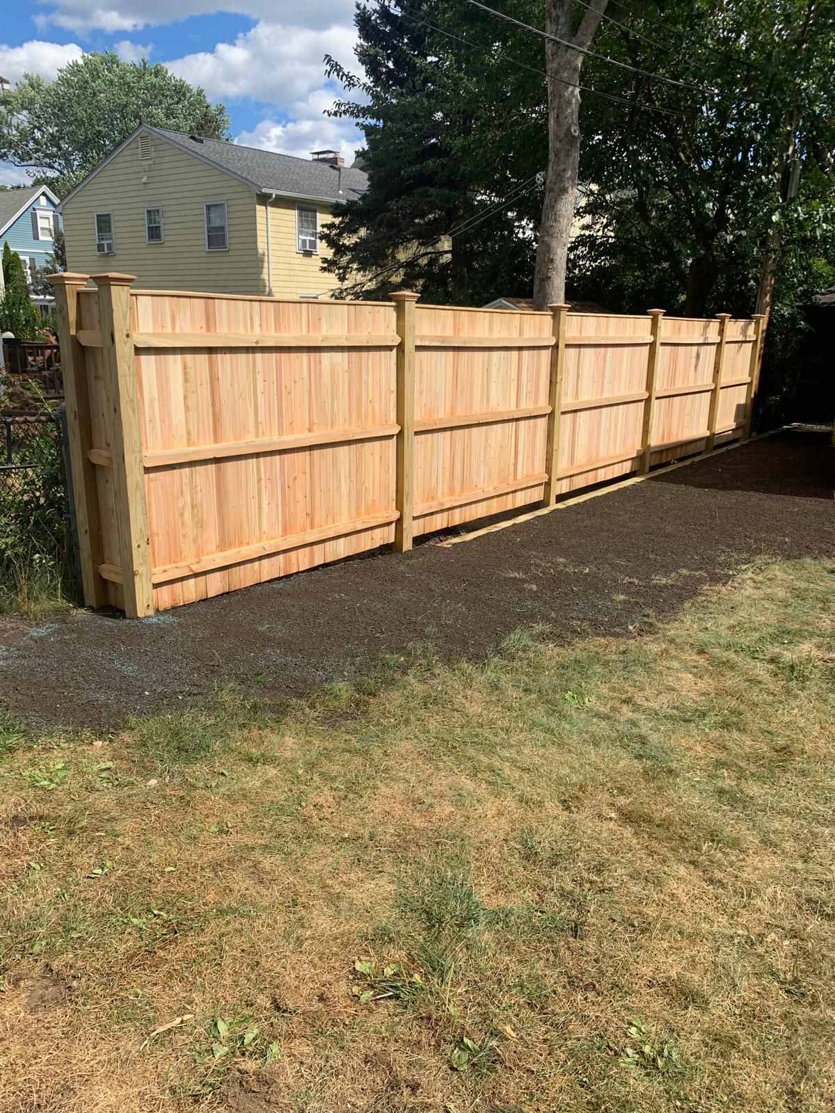 New wooden privacy fence along a grassy yard with houses and trees in the background