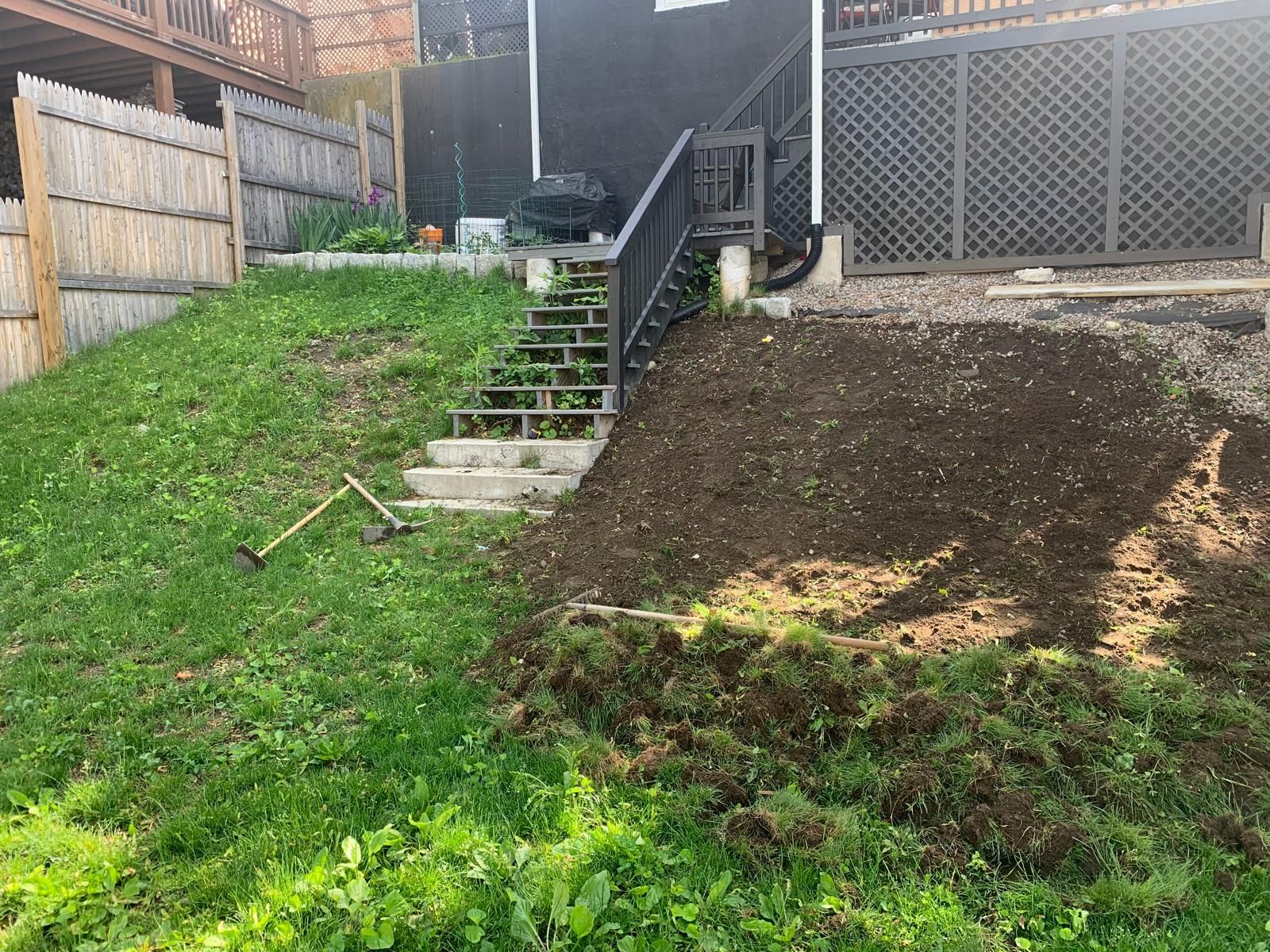 Backyard slope with grassy and bare dirt sections, stone steps, and a wooden fence beside a deck