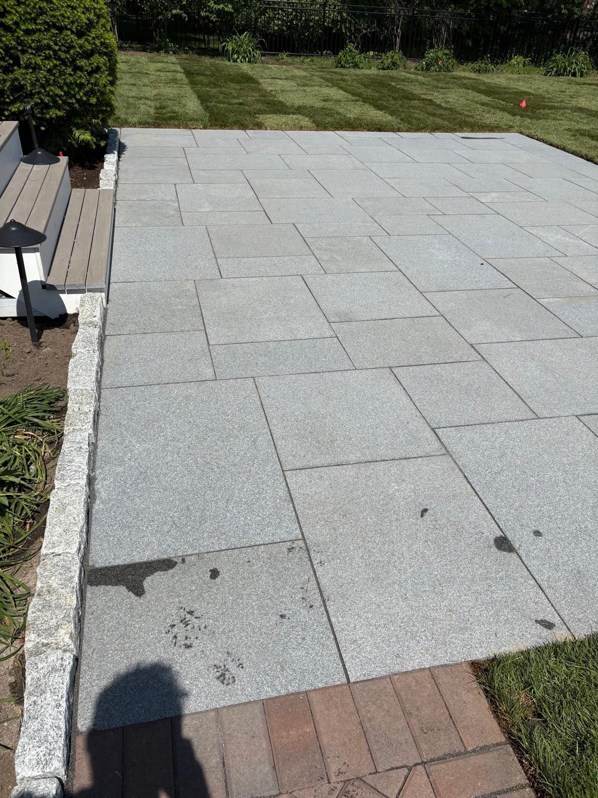 Gray paver patio bordered by grass, with a bench and steps on the left side