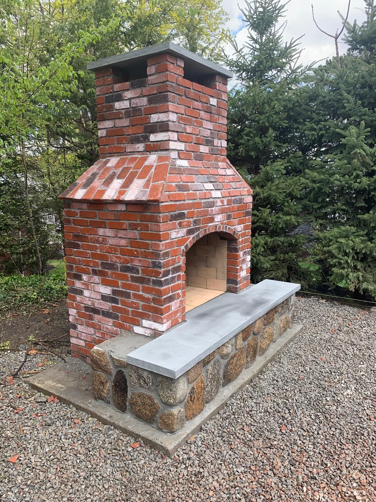 Brick outdoor fireplace with chimney and stone bench in a gravel yard