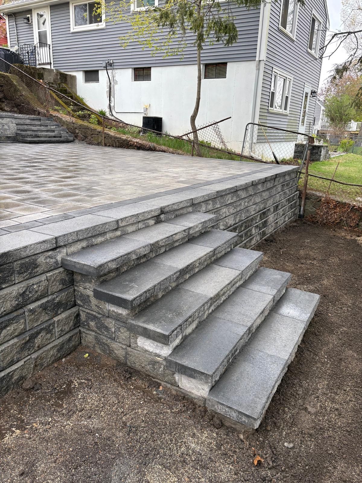 Stone outdoor stairs beside a raised driveway and white house siding