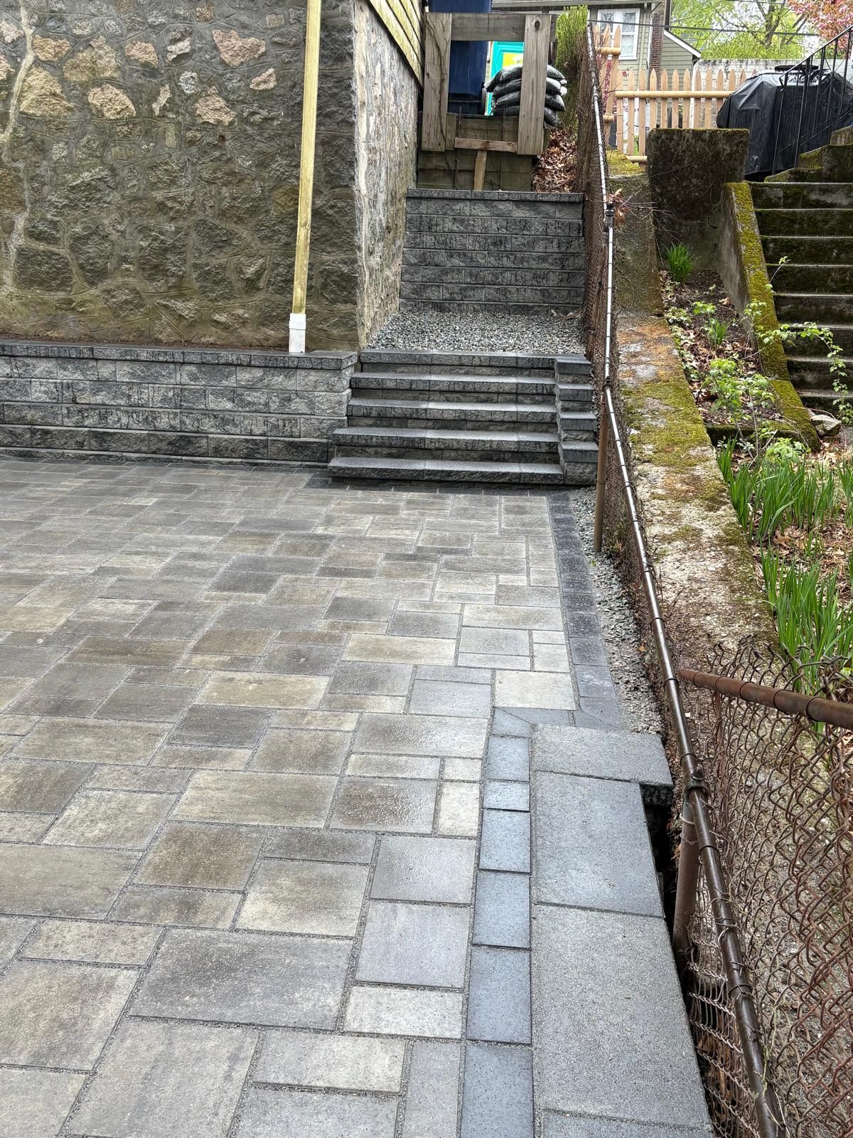 Stone steps between brick walls leading up from a paved courtyard with a narrow garden on the right