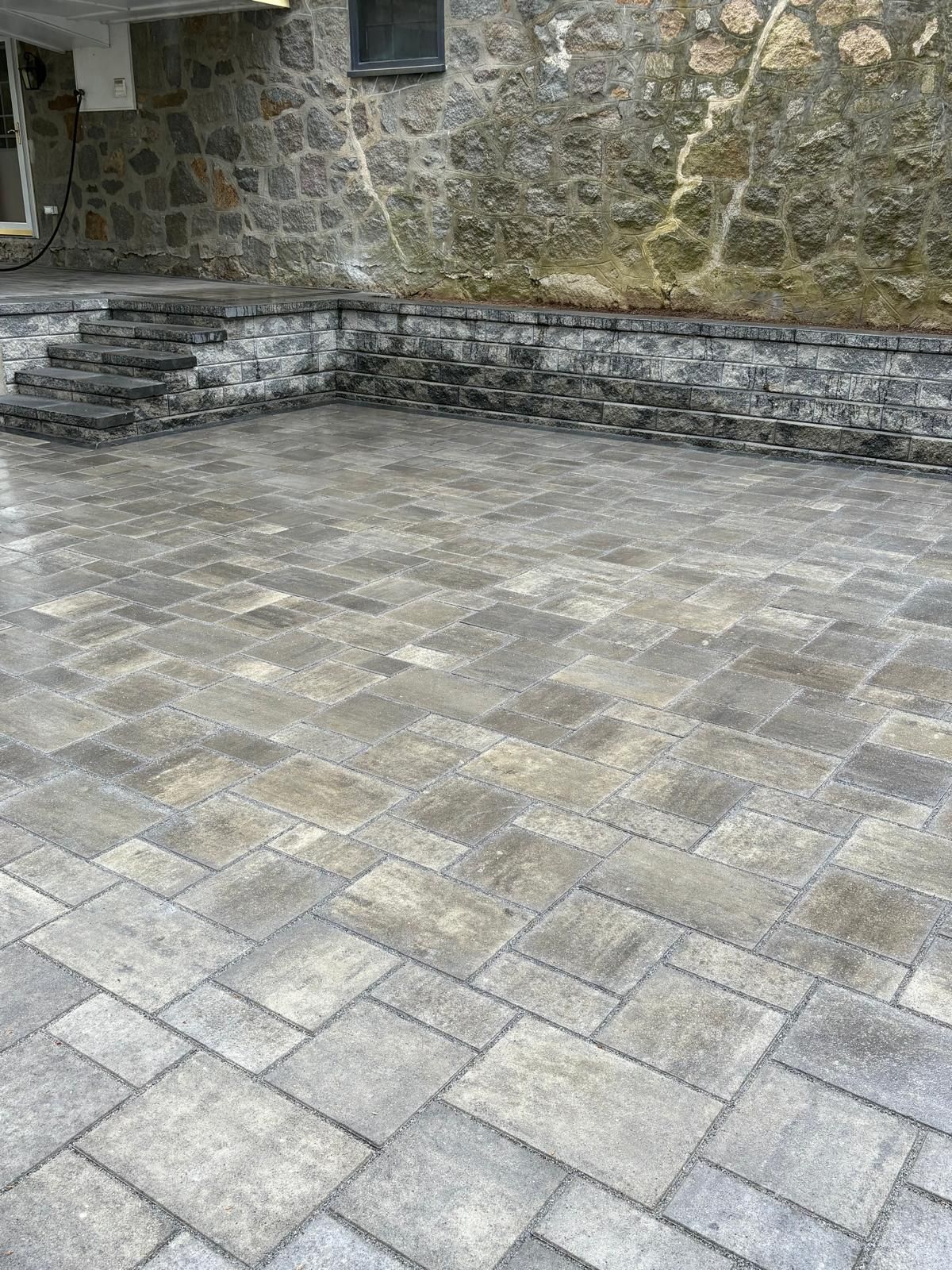 Stone courtyard with gray pavers, steps, and a mossy stone wall