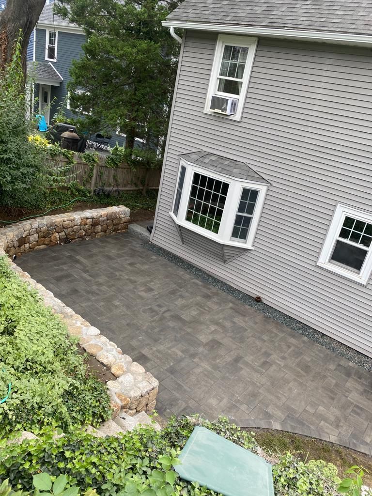 Gray house exterior with stone-bordered driveway, green shrubs, and neighboring homes in a residential area