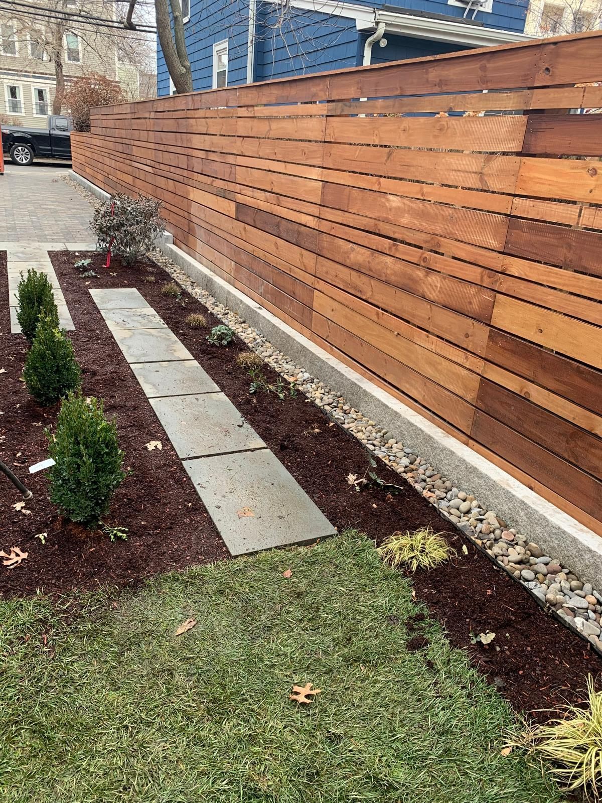 Landscaped yard with wooden fence, concrete stepping stones, mulch, shrubs, and grass.