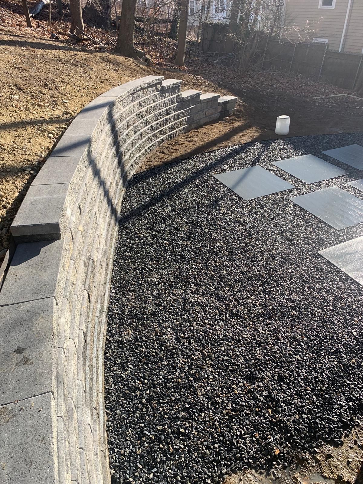 Curved stone bench beside a gravel patio with stepping stones in a landscaped yard