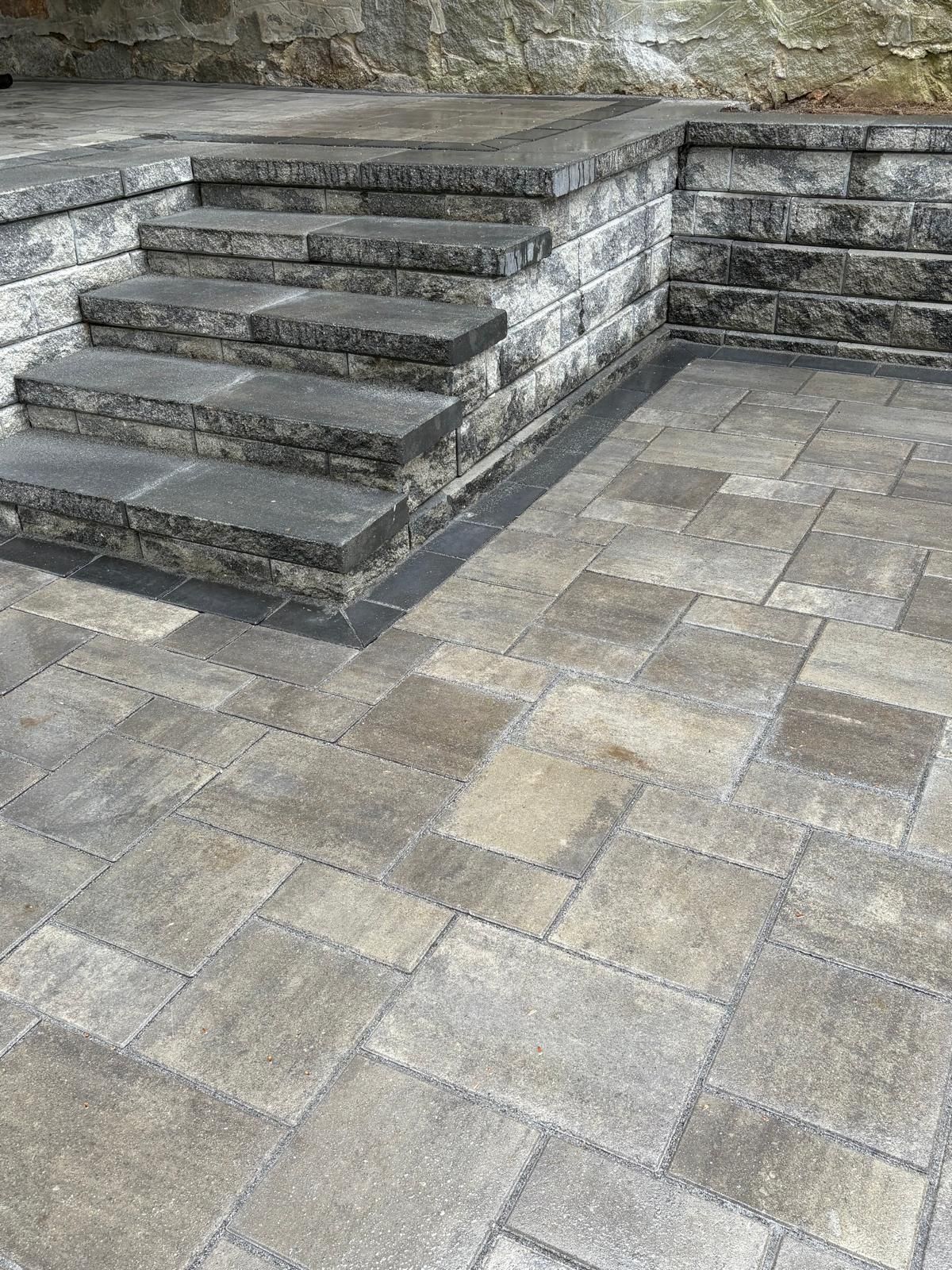 Stone steps beside a paved courtyard with gray tiles and a low retaining wall