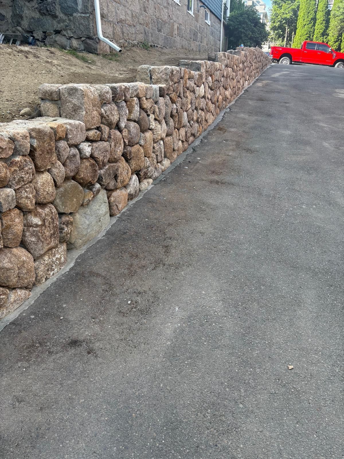 Stone retaining wall along a steep paved road, with a red car parked at the top right.