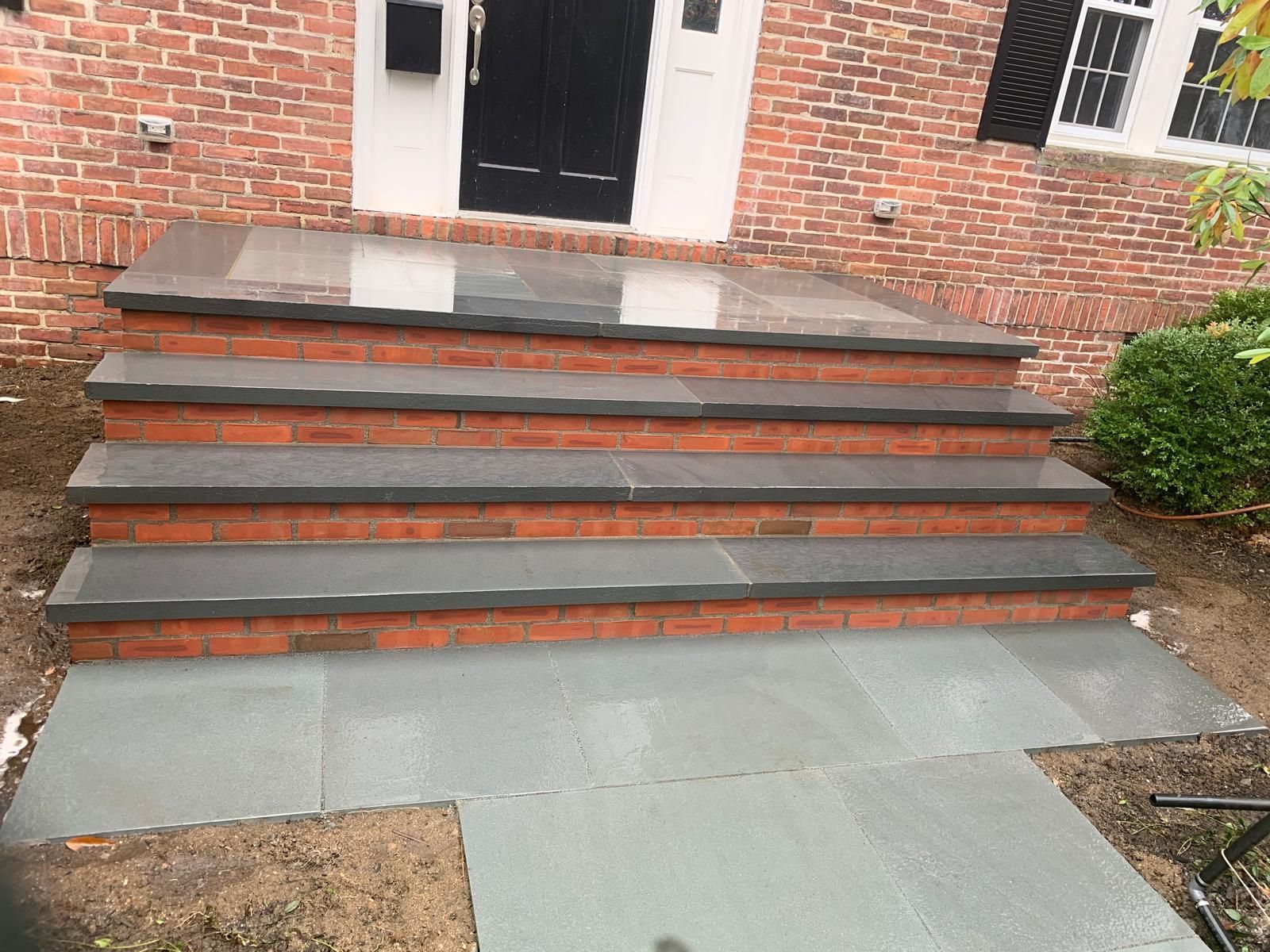Brick front steps with gray concrete treads leading to a white doorway and walkway