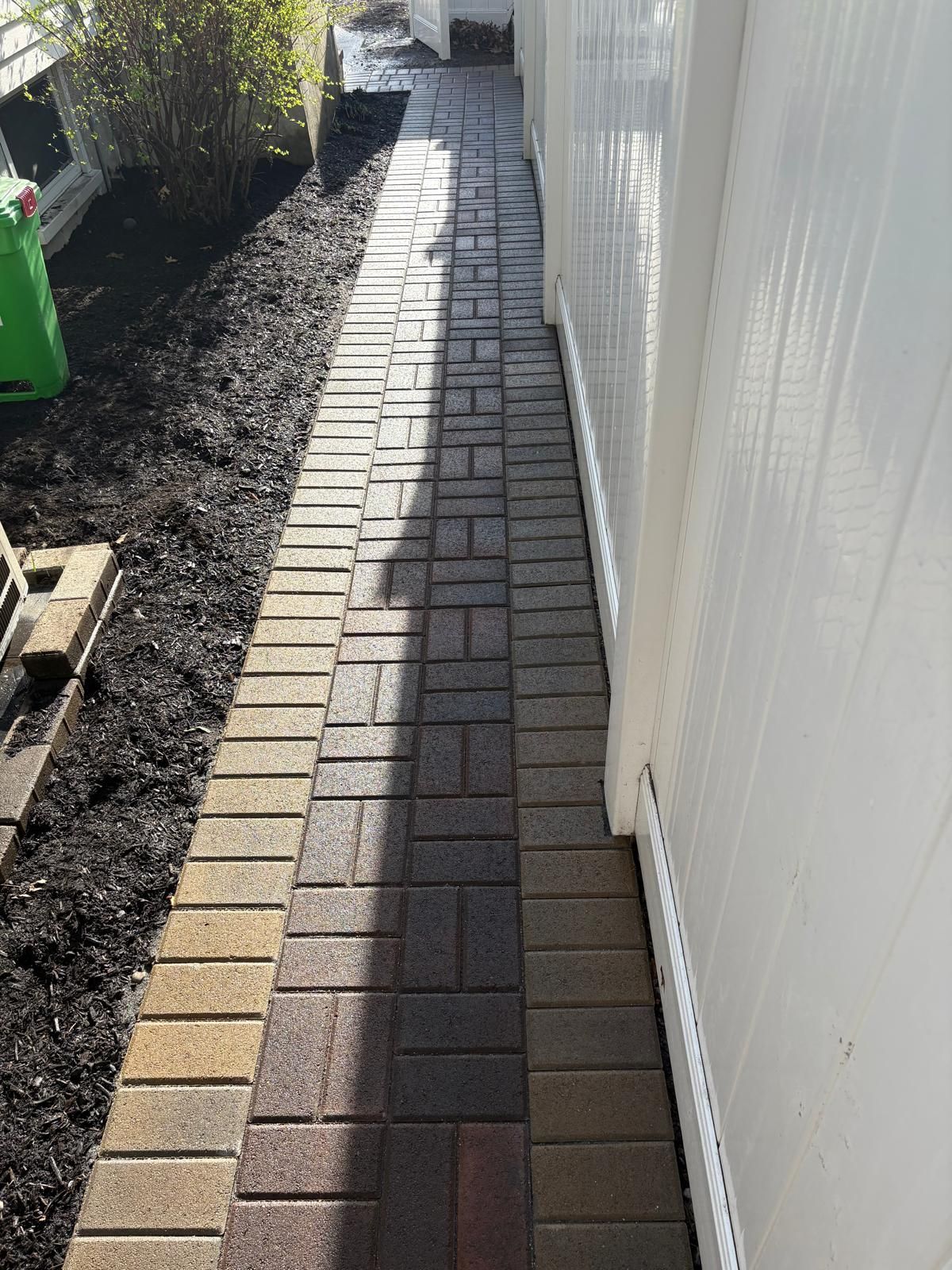 Narrow brick paver walkway beside a white fence in a yard, with long shadows and soil edging.
