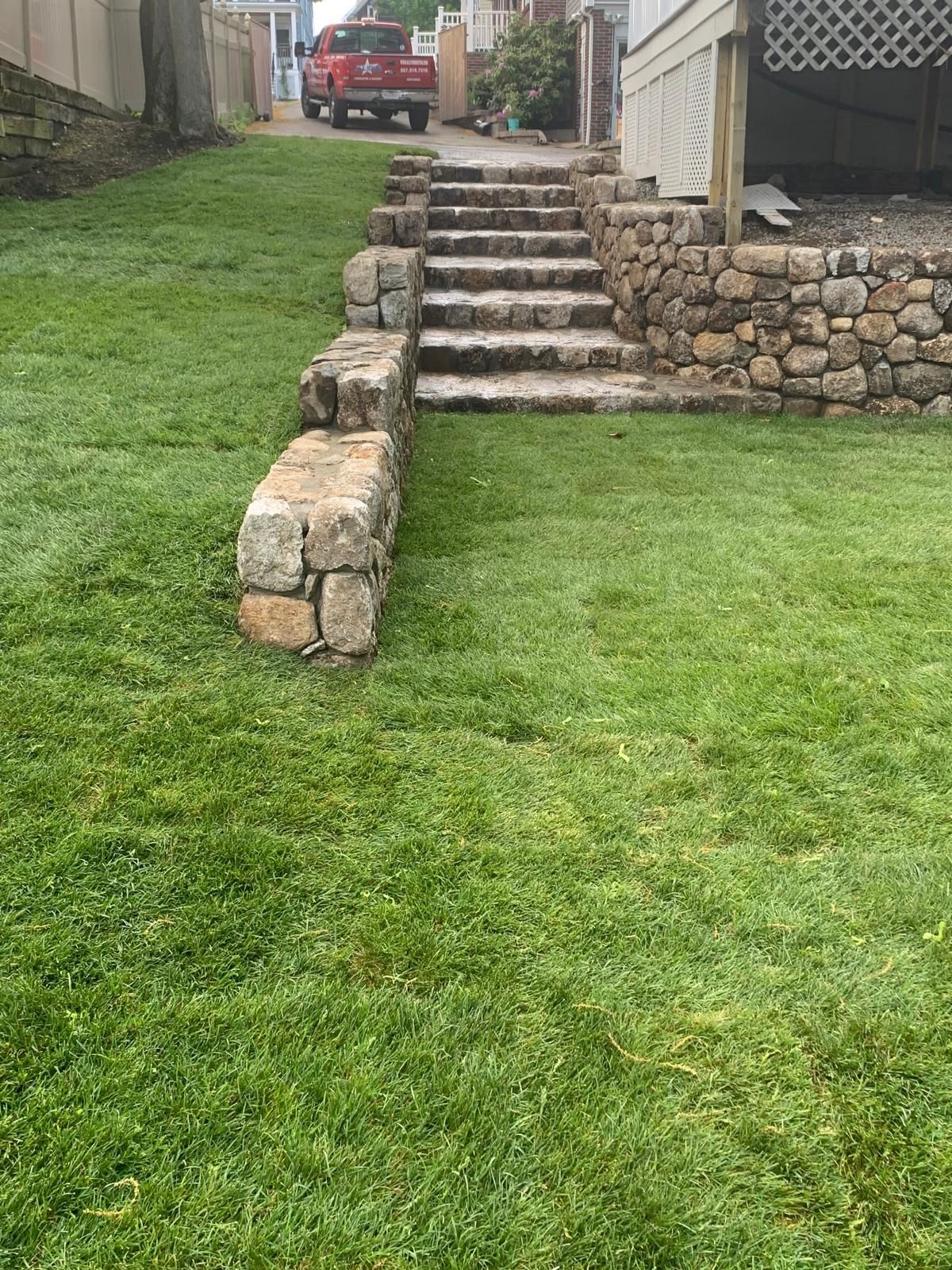 Stone steps leading up a grassy slope to a red truck in a driveway, with stone retaining walls.