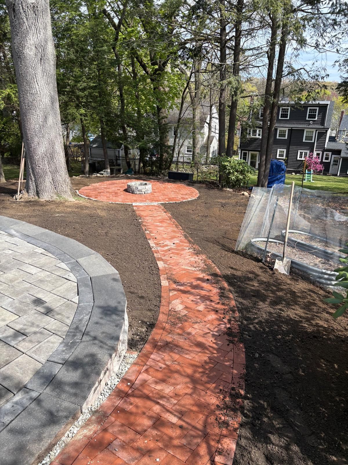 Curved orange path in a wooded park beside a paved walkway and fenced area
