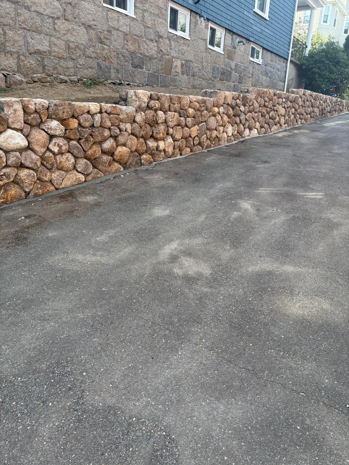 Steep paved road beside a stone retaining wall and blue building