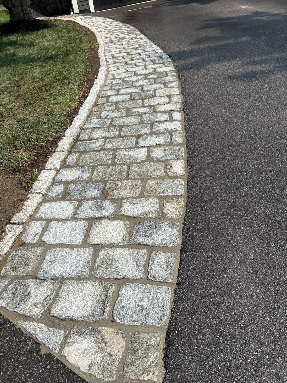 Curved cobblestone path beside dark asphalt road and grassy edge