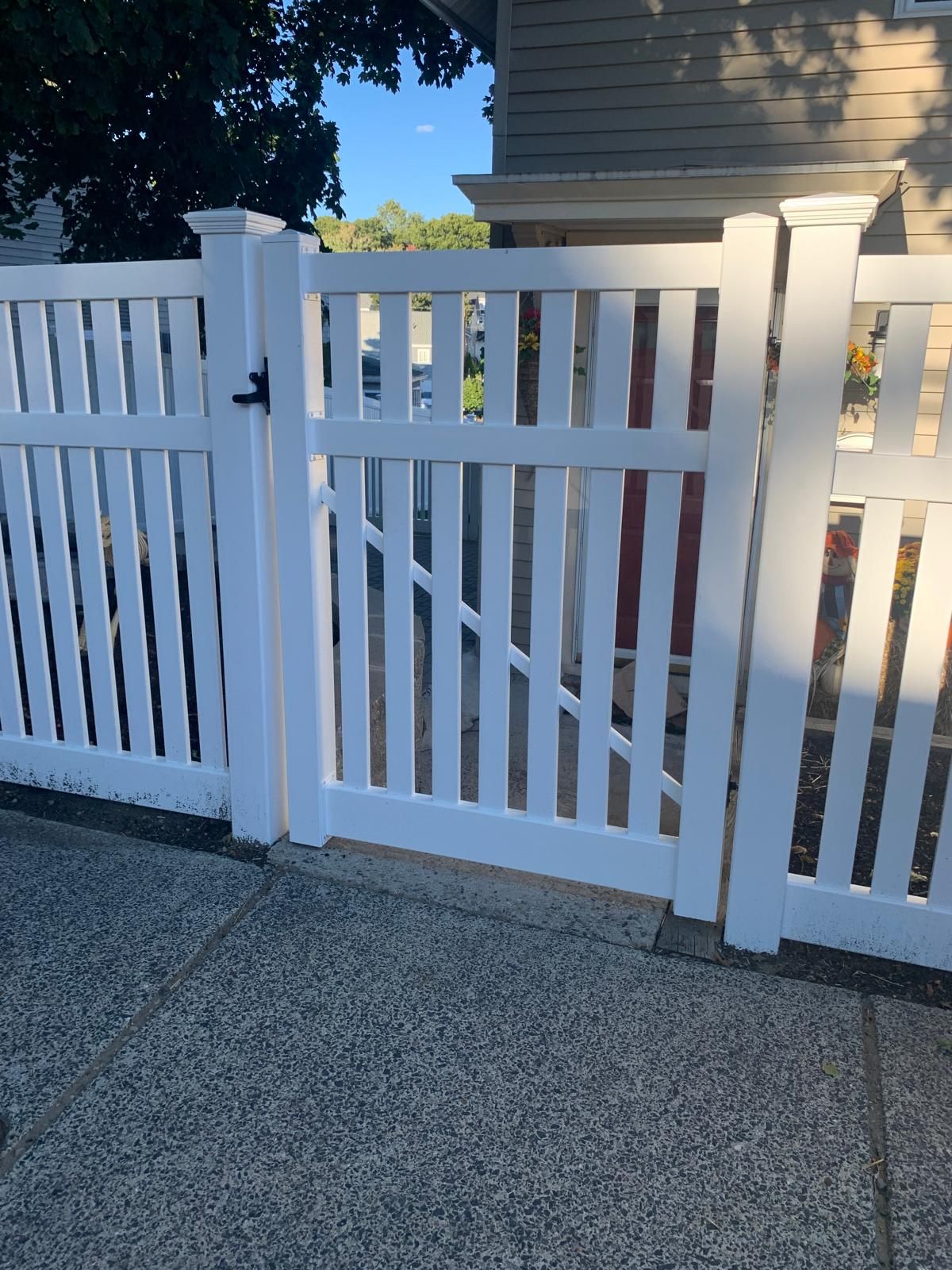 White vinyl gate in a picket fence beside a house, opening onto a concrete walkway.