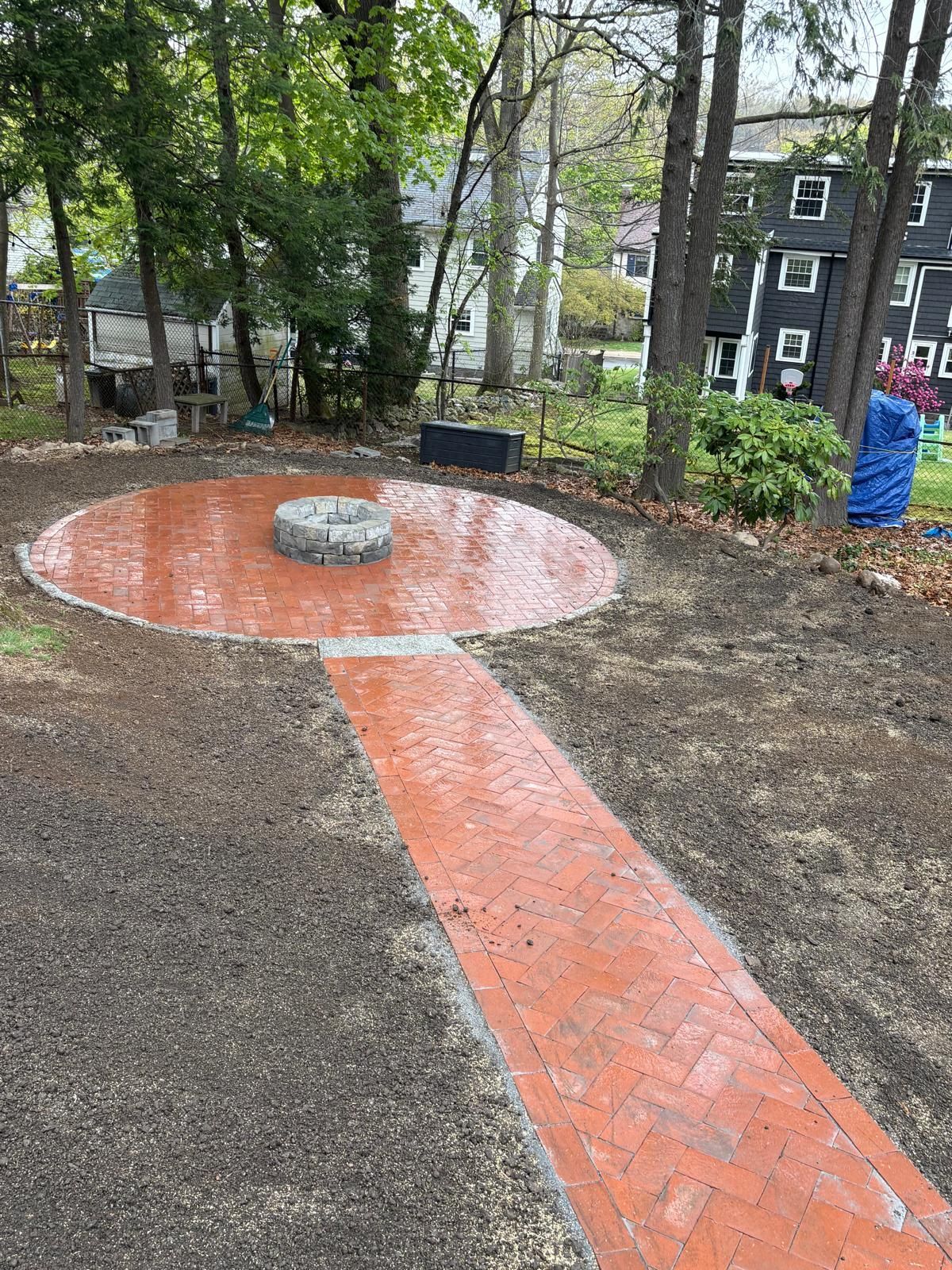 Brick path leads to a circular patio with a stone bench in a wooded courtyard.