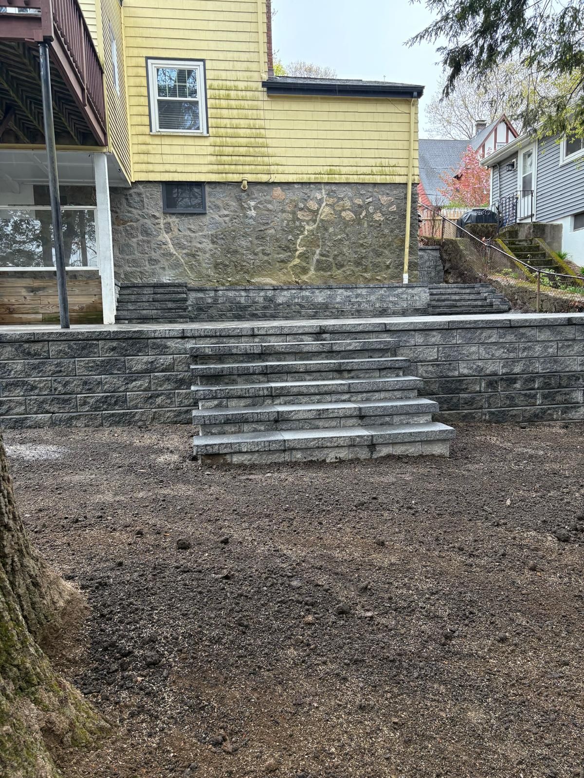 Stone steps lead up to a yellow house with a retaining wall and gravel yard