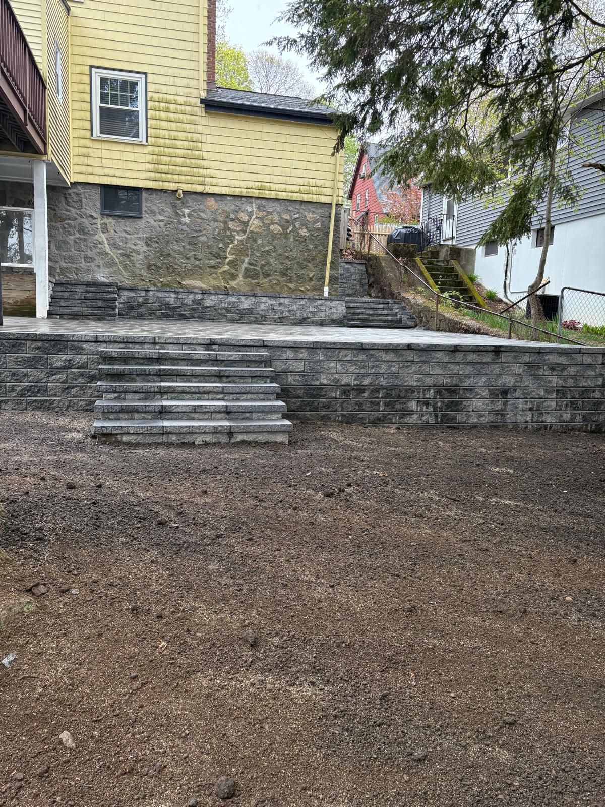 Stone steps leading up to a yellow house beside a gravel yard and trees