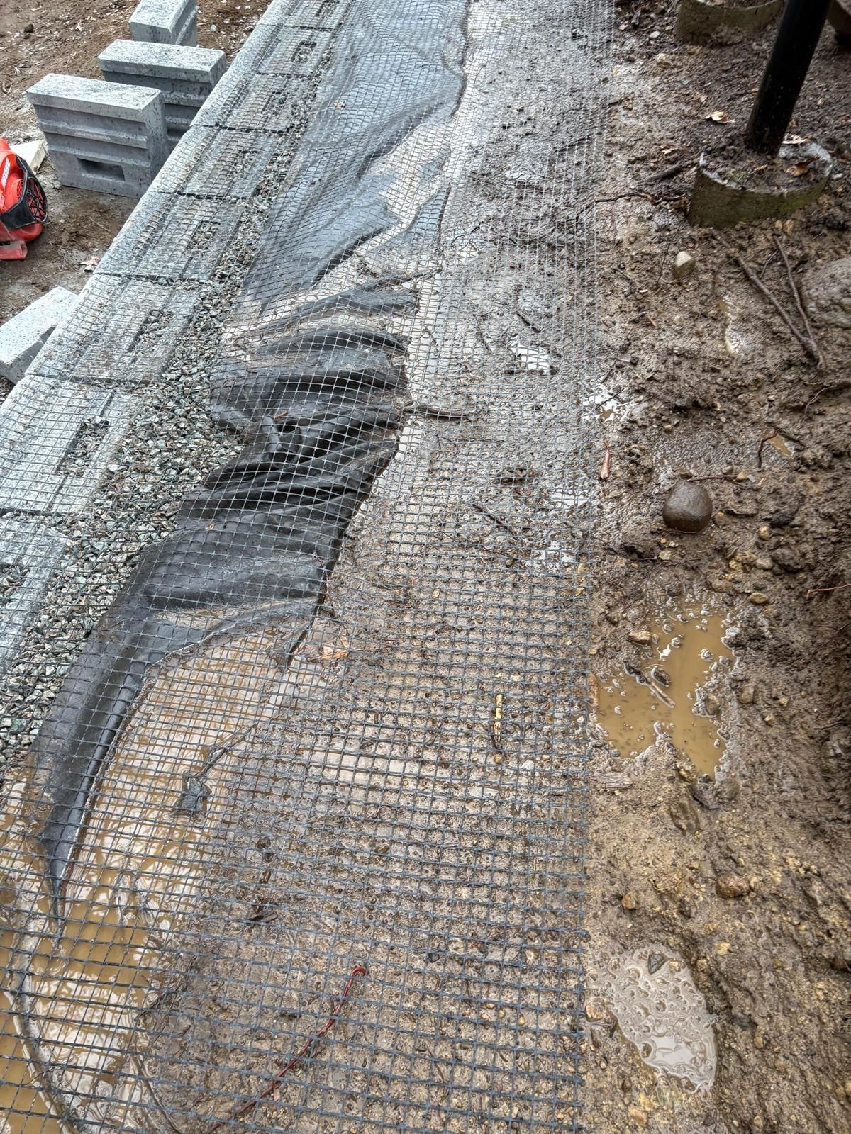 Wet construction mesh on a muddy roadside embankment with puddles and exposed gravel