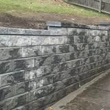 Stone retaining wall along a sloped path with a grassy hillside above and concrete edge below