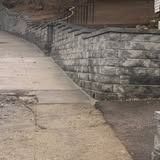 Stone retaining wall beside a sloped concrete path on a street corner