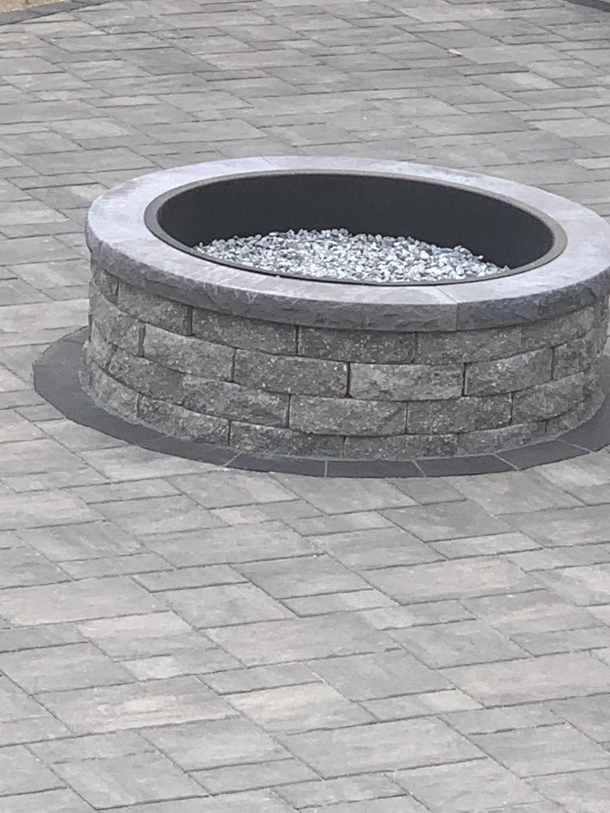 Round stone fire pit filled with gravel on a paved patio