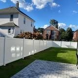 Backyard with white fence, green lawn, and gray stone patio beside a house
