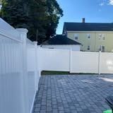 White fenced backyard with gray pavers, trees, and a pale yellow house in the background